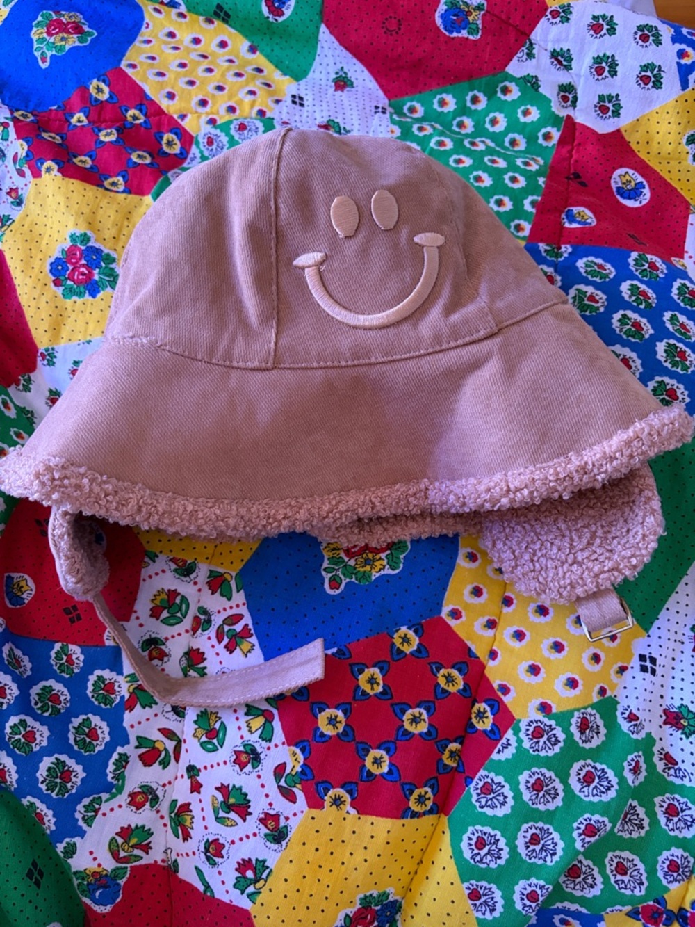 Tan corduroy smiley face bucket hat, a sherpa fleece lining with earflaps.